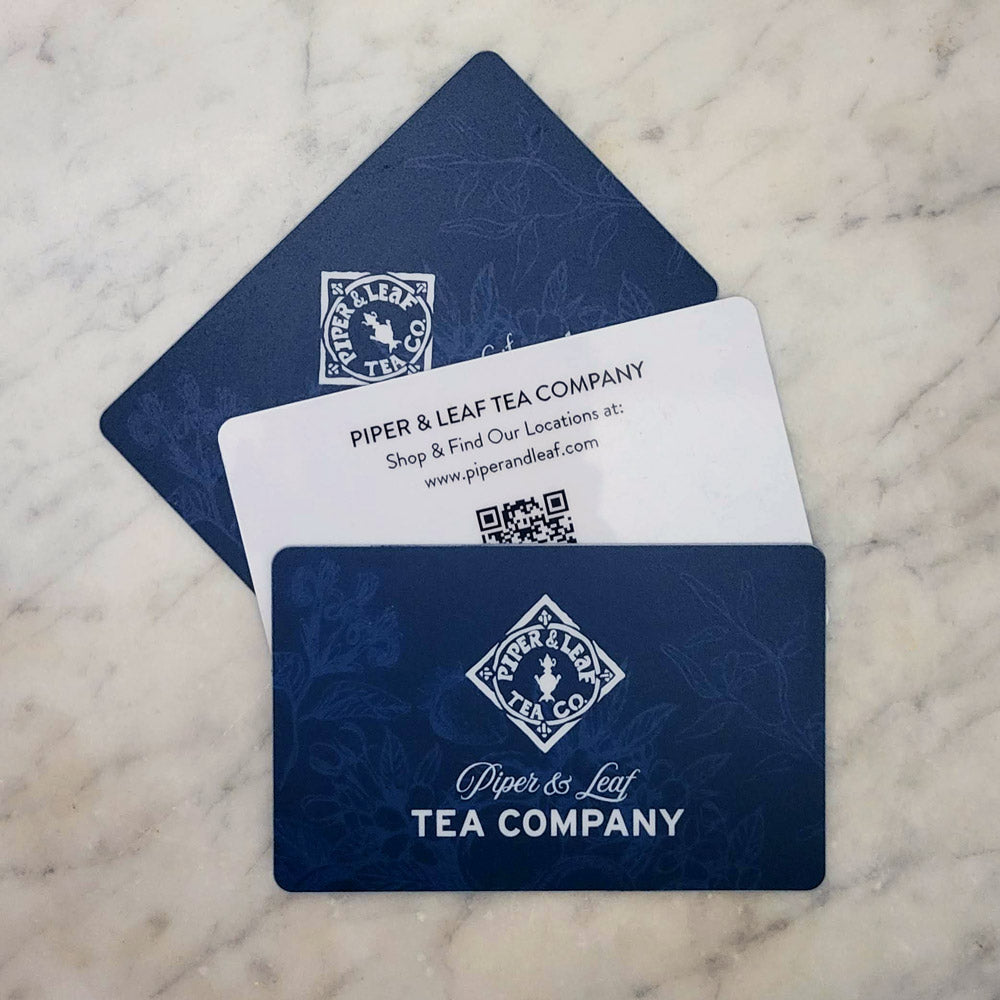 A trio of blue gift cards with berries, flowers, & herbs beneath the Piper & Leaf logo. Front: "Piper & Leaf Tea Company" Back: "Shop & Find Our Locations at: www.piperandleaf.live"
