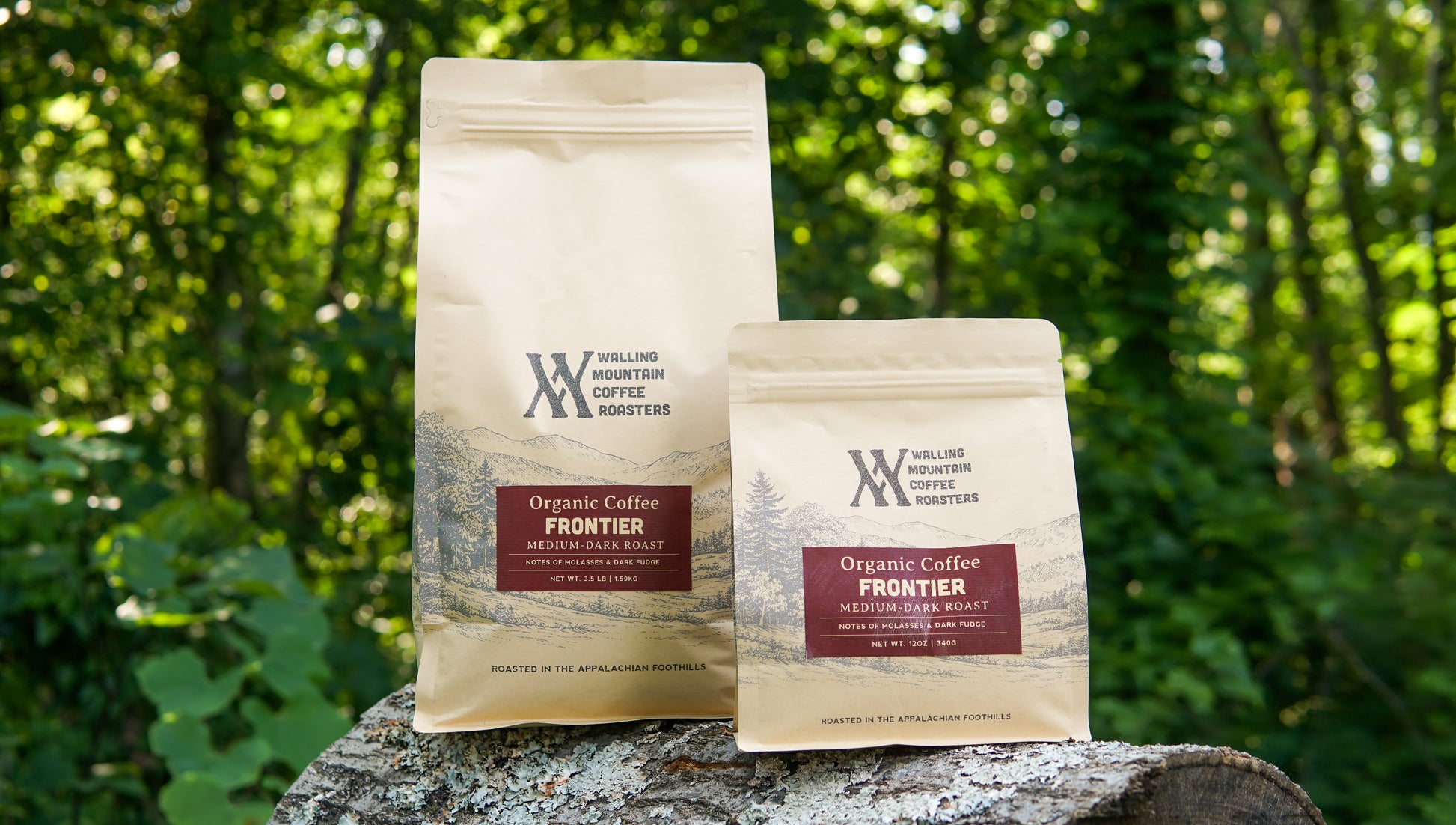 Two 3.5lb bags of Walling Mtn. Coffee, labeled "Frontier Roast Organic Coffee," are displayed outdoors on a tree stump with green foliage in the background. This rich organic blend is expertly crafted by Walling Mtn. Coffee using traditional roasting methods for an authentic and bold flavor experience.