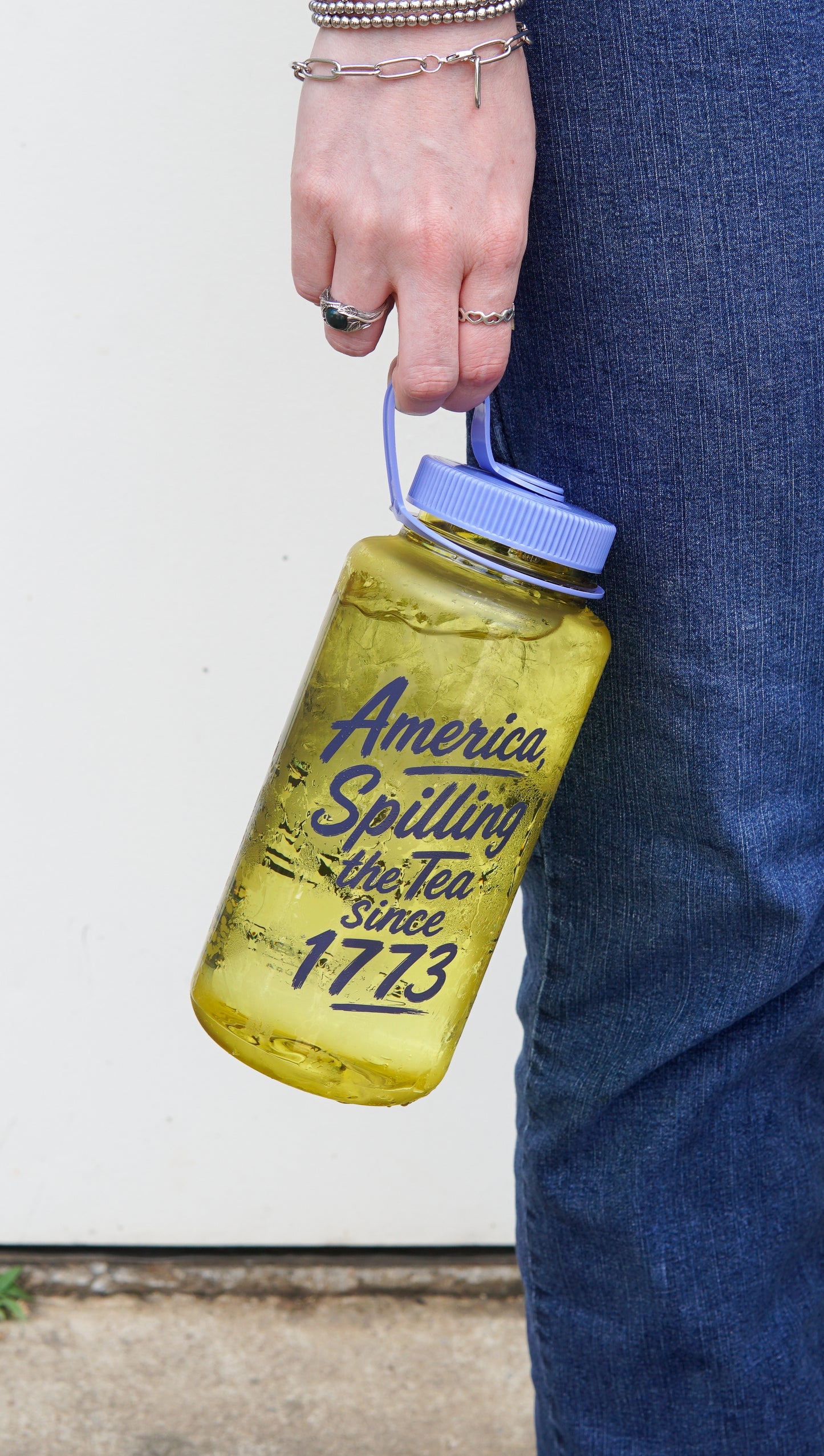 Someone in jeans holds a yellow drink in a Piper and Leaf Tea Co. “Spilling the Tea Nalgene” bottle.