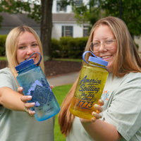 Two young women outdoors smile at the camera, each holding a large water bottle featuring printed tea-spilling designs and 
