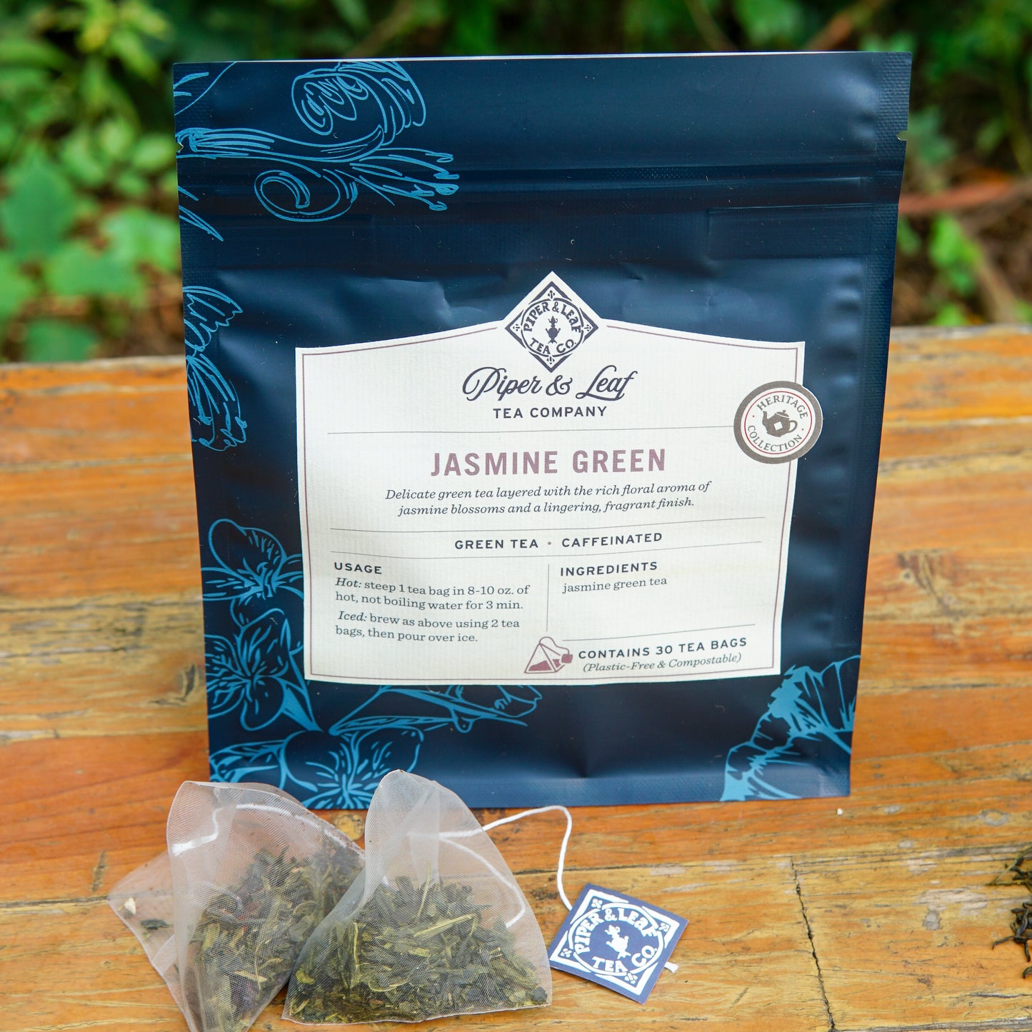A bag of Piper and Leaf Tea Co. Jasmine Green 30ct Tea Bags rests on a wooden surface, accompanied by two tea bags and a tea tag displayed in front.