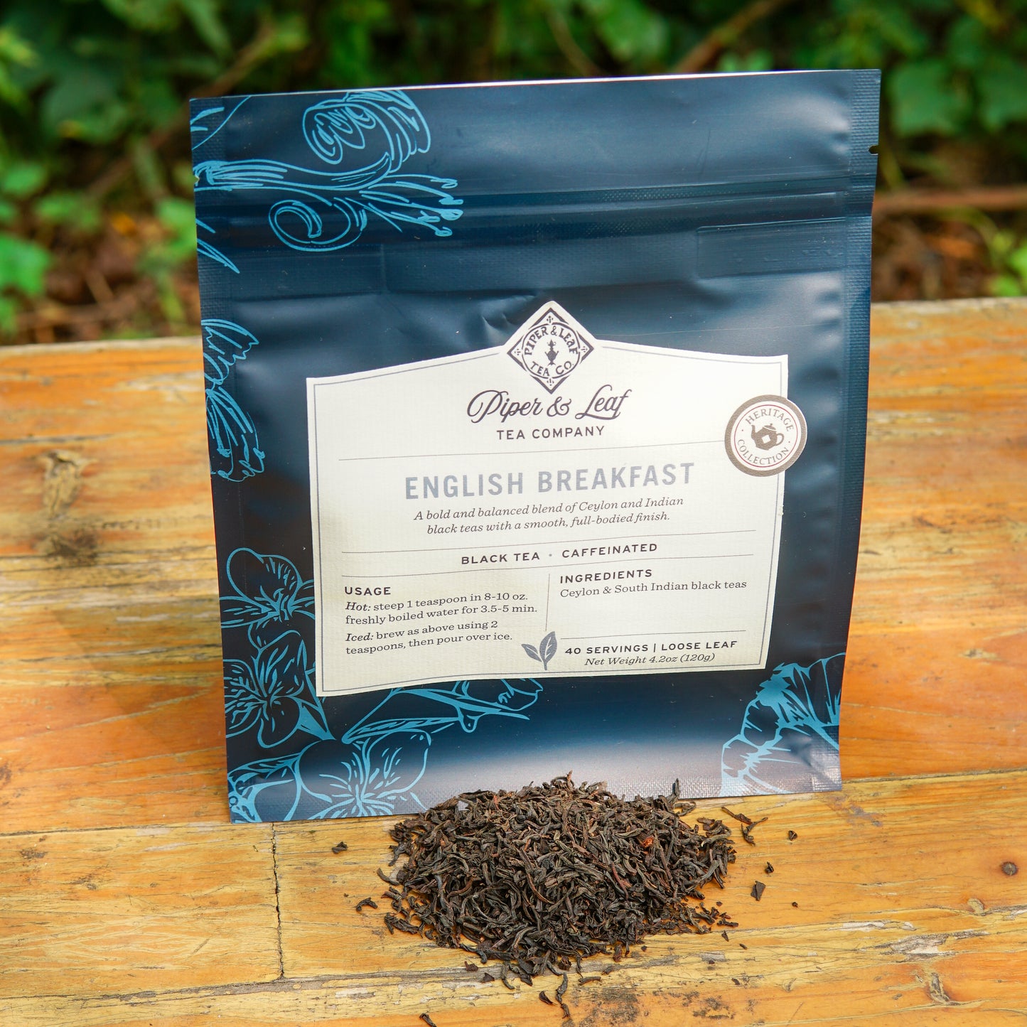A bag of Piper and Leaf Tea Co. English Breakfast 40 Serving Loose Leaf is displayed on a wooden surface with loose leaf tea scattered in front, highlighting the rich Ceylon black tea blend inside.
