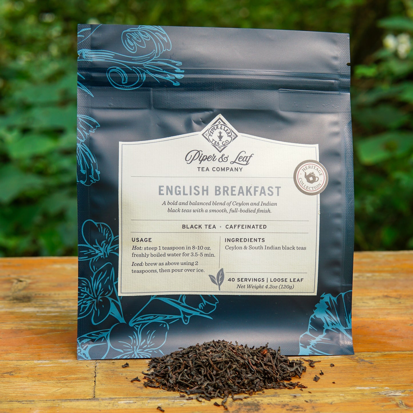 A blue bag of Piper and Leaf Tea Co. English Breakfast 40 Serving Loose Leaf is displayed outdoors, with a small pile of Ceylon black tea leaves arranged in front of the bag.
