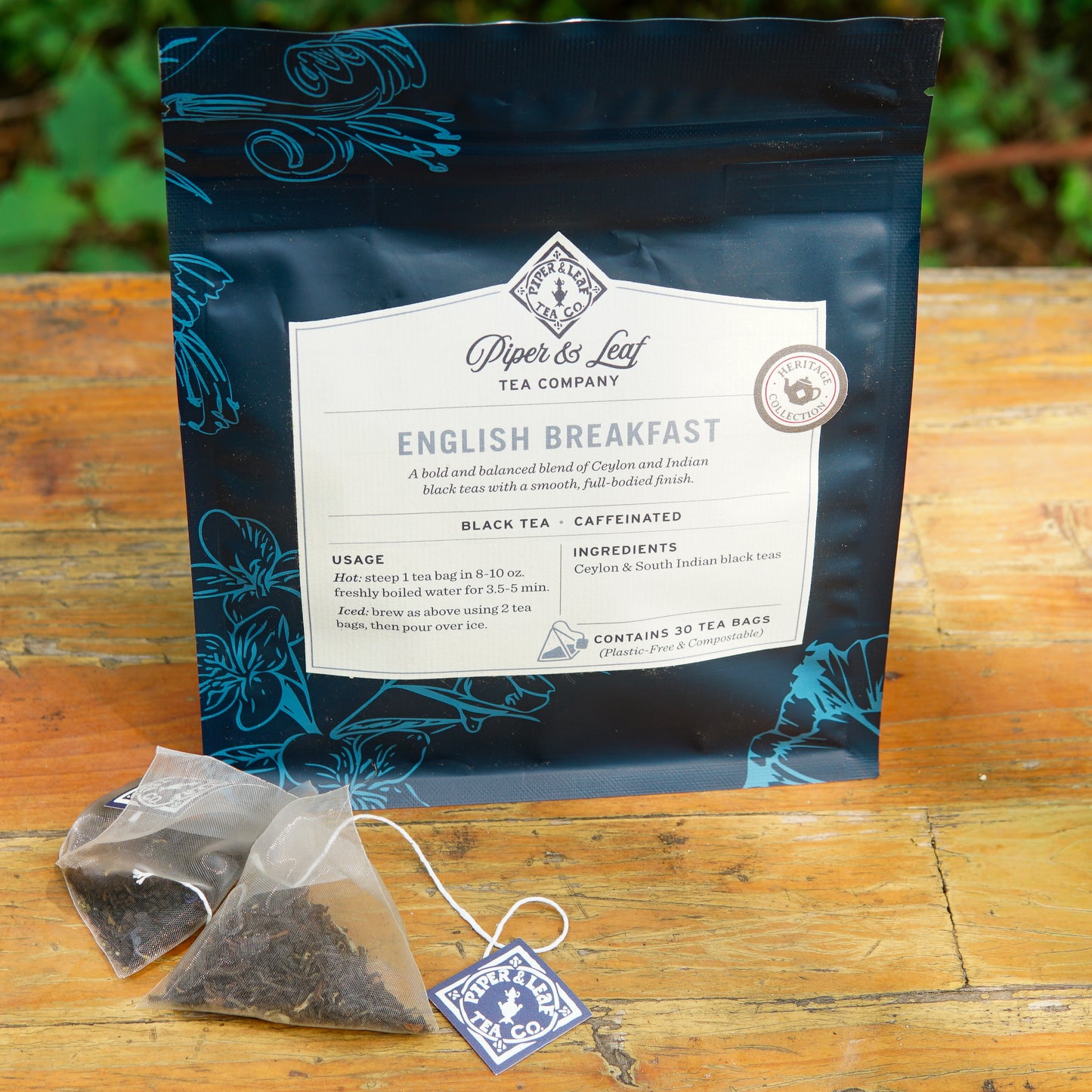 A bag of Piper and Leaf Tea Co. English Breakfast 30ct Tea Bags rests on a wooden surface, with two pyramid tea bags and a branded tag placed in front of it.