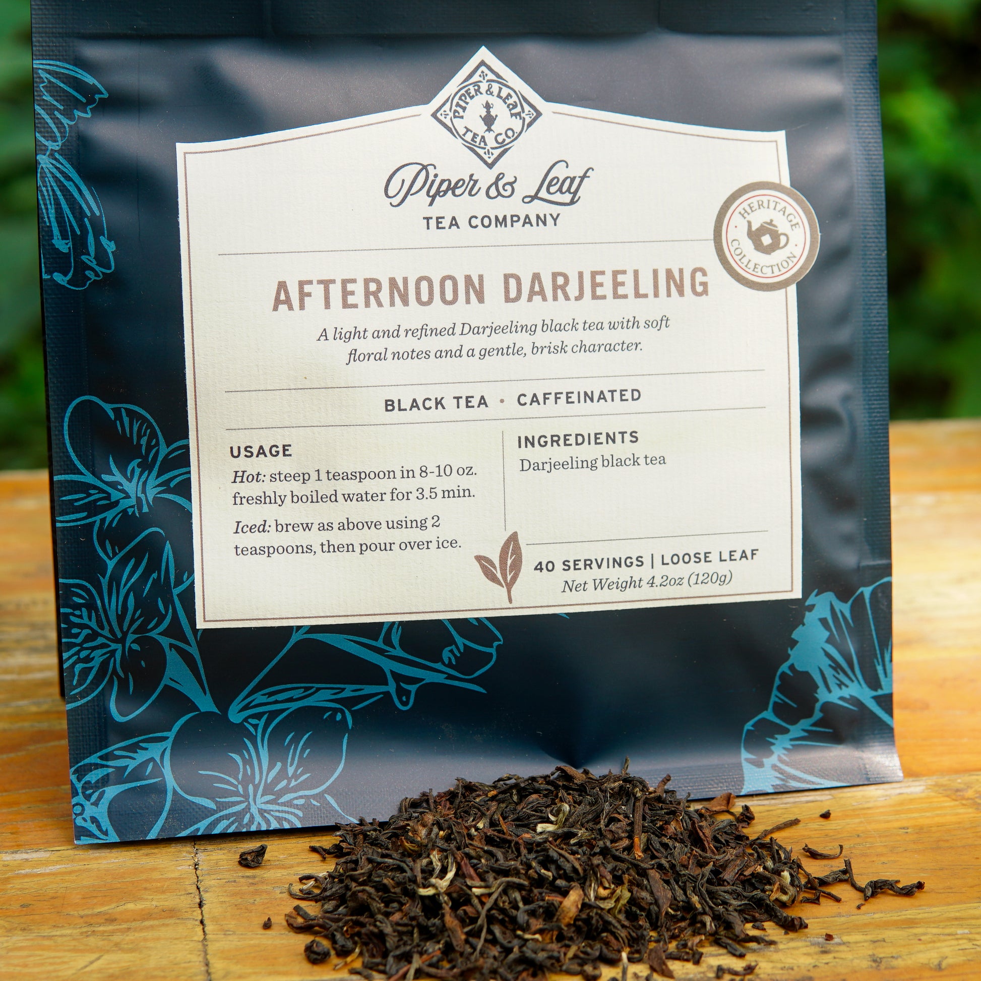 A bag of Piper and Leaf Tea Co. Afternoon Darjeeling 40 Serving Loose Leaf tea rests on a wooden surface, with loose-leaf tea scattered in front.