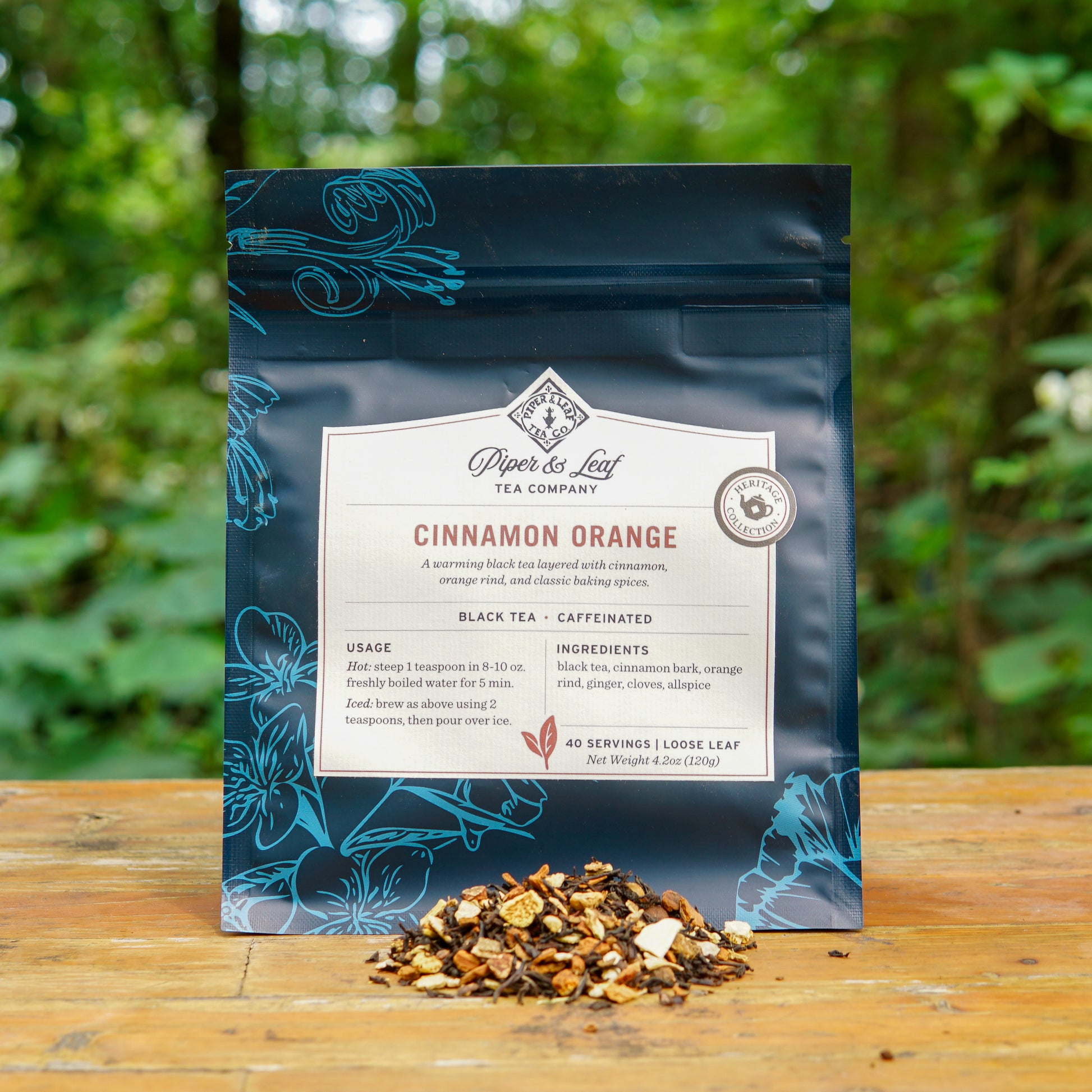 A bag of Piper and Leaf Tea Co. Cinnamon Orange 40 Serving Loose Leaf Tea sits on a wooden surface outdoors, with aromatic loose leaf tea displayed in front of the package.
