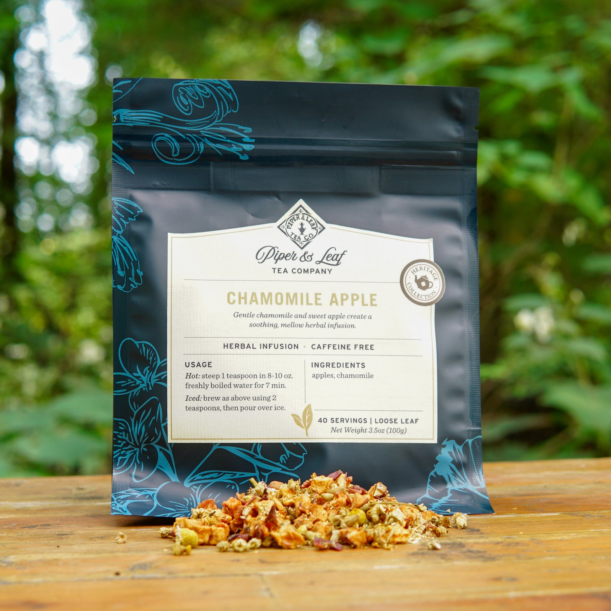 A bag of Piper and Leaf Tea Co.’s Chamomile Apple 40 Serving Loose Leaf Tea rests on a wooden surface outdoors, with dried tea leaves scattered in front, highlighting this soothing caffeine-free herbal infusion.