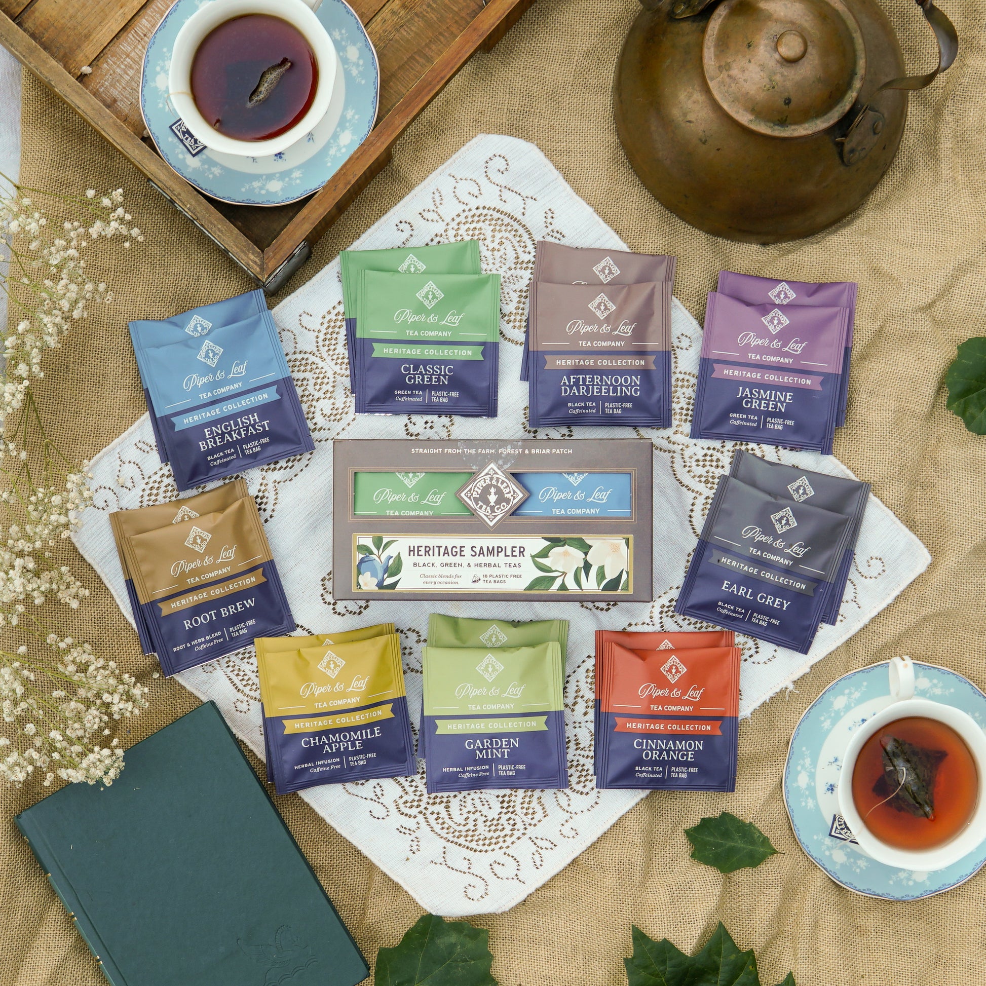 Heritage Sampler box on a lace and burlap backdrop surrounded by dried flowers, book, and tea