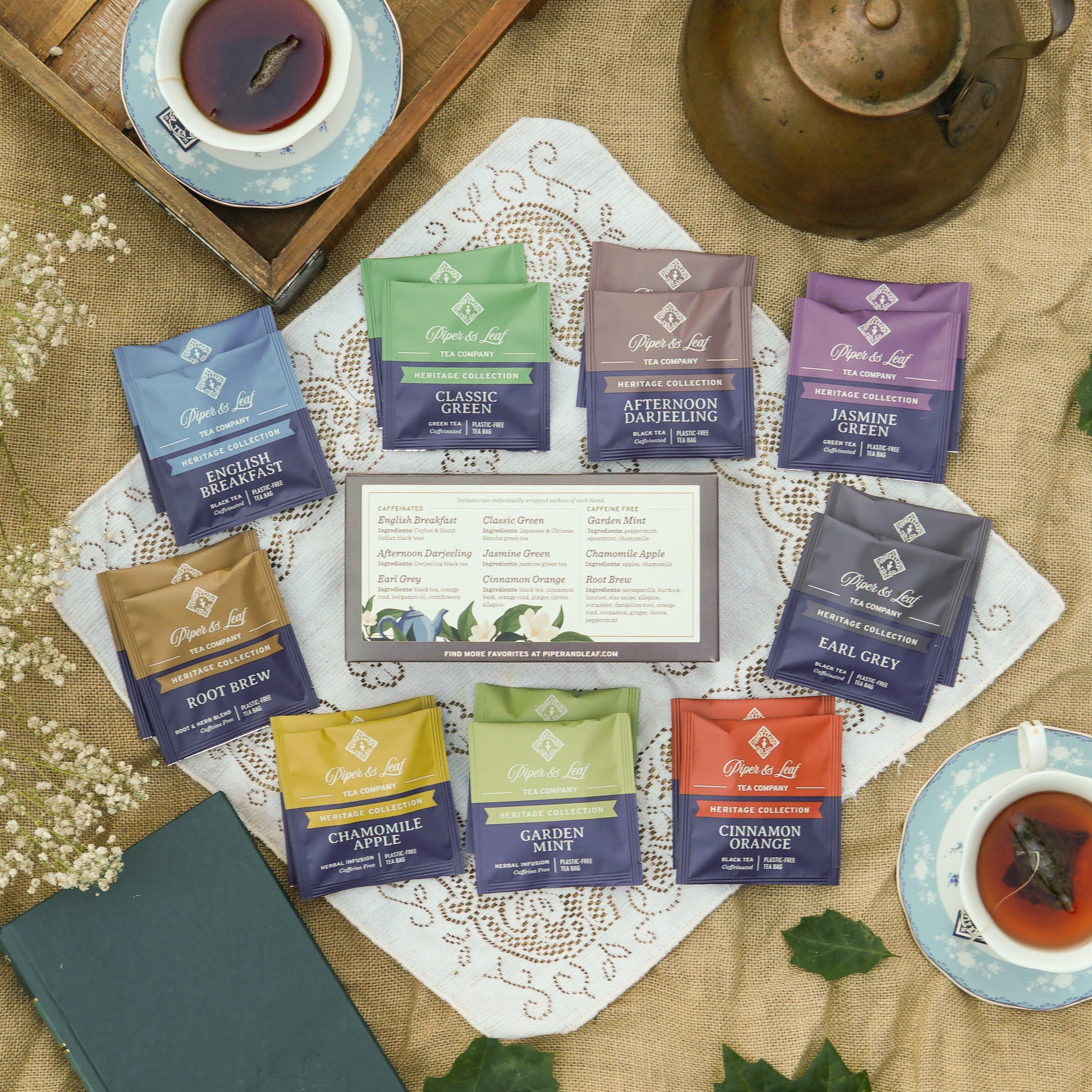 A styled flat-lay of Opal Leaf tea blends arranged on a lace doily over burlap fabric, with a tea tray, teapot, cups of tea, and small flowers around the product packets. The center shows a branded tea box with multiple single-serve packets in different colors and flavors.