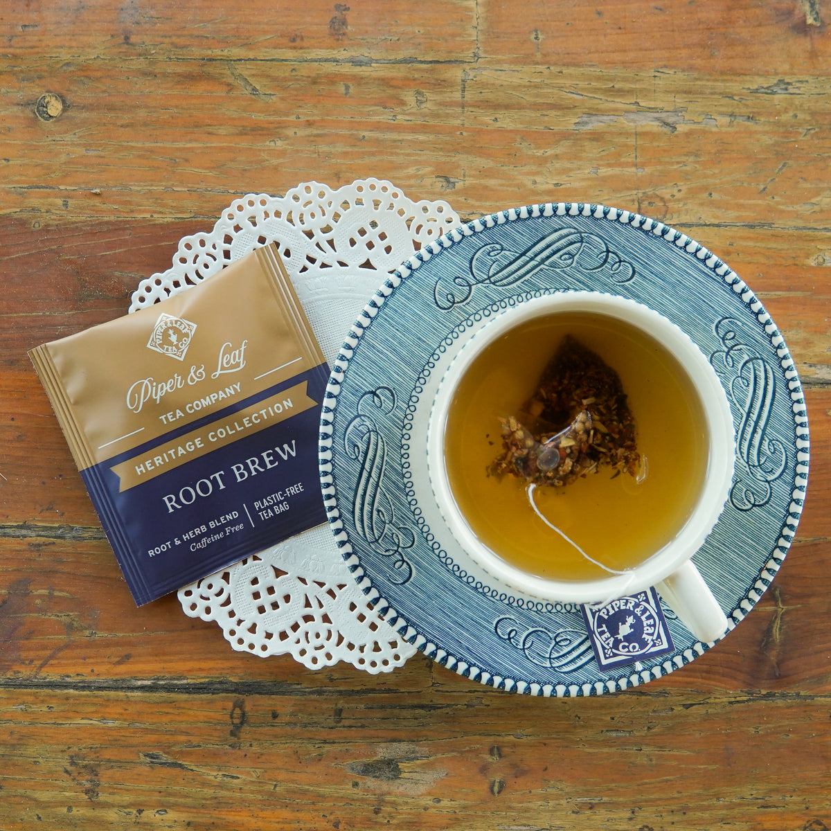 A Piper and Leaf Tea Co. “Root Brew” 50ct Individually Wrapped Tea Bag from the Heritage Collection rests on a wooden surface. The package is brown and navy, adorned with white and gold lettering.