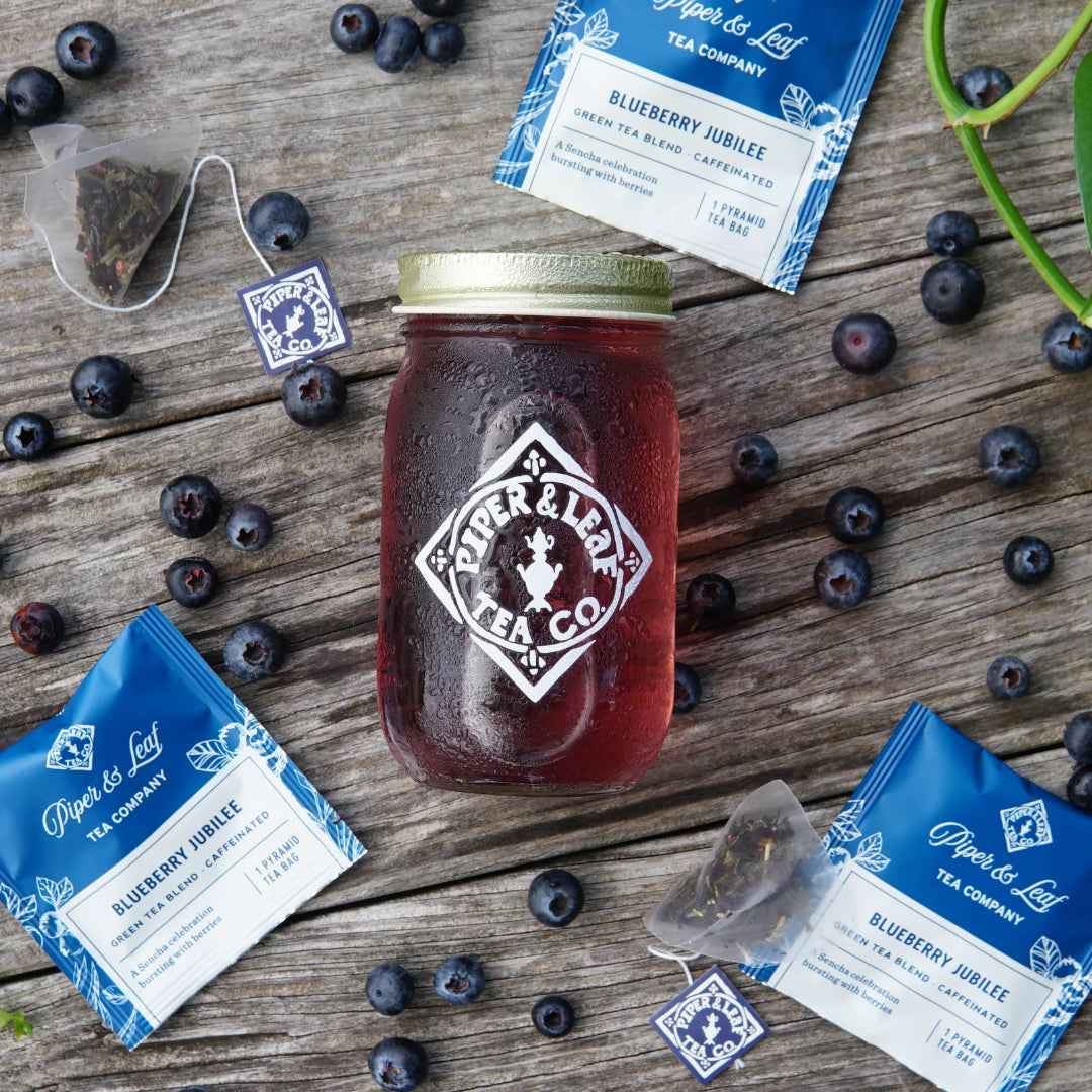 Jar of Blueberry Jubilee next to  single packages on a wooden surface with blueberries.